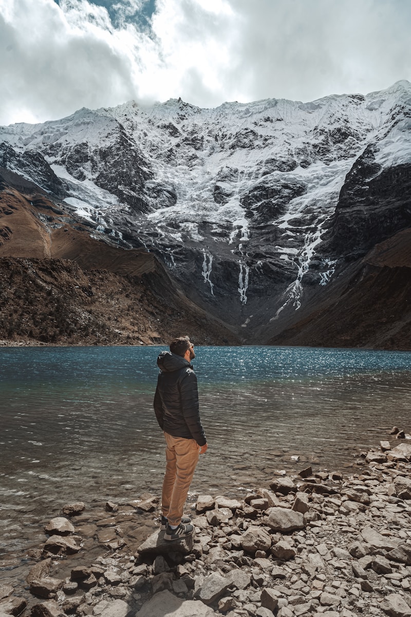 a man standing on a rocky shore with a mountain in the background